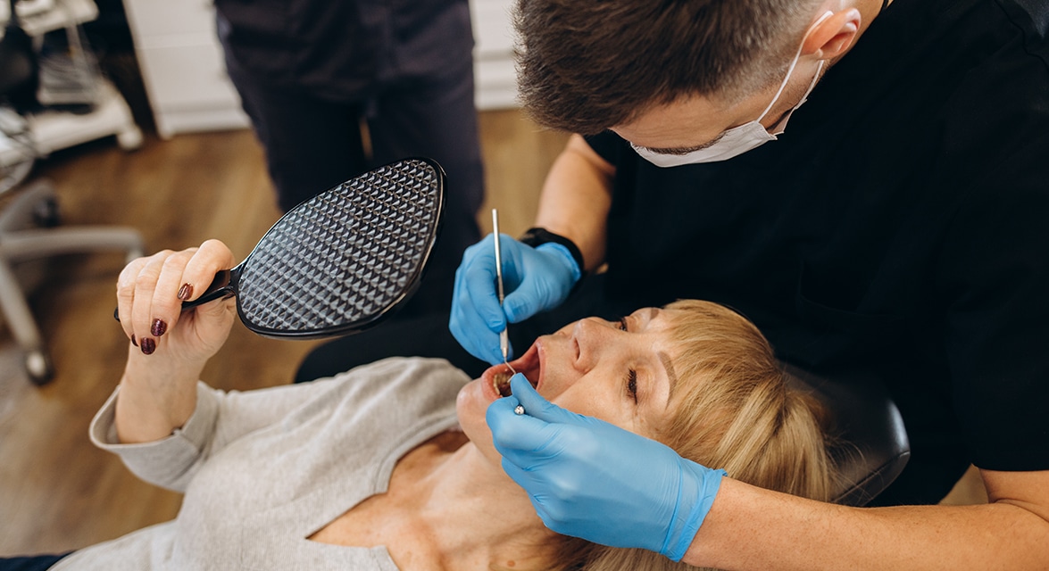 Elderly woman examining her teeth in the mirror, showcasing a moment of self-care and reflection