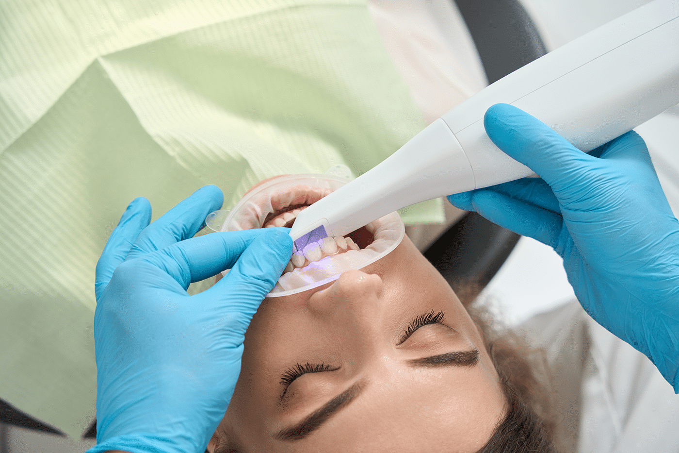 A woman undergoing a teeth cleaning procedure with UV light, showcasing a bright and modern dental environment